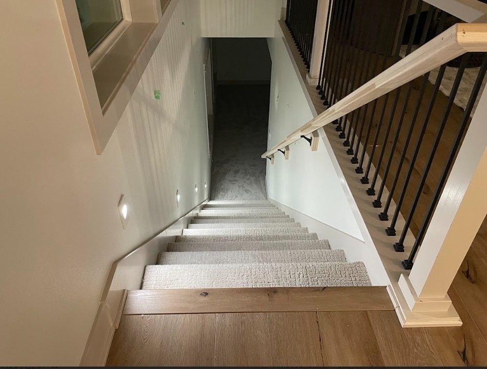 Staircase with light-colored carpet, white walls, and a dark, carpeted landing at the bottom.