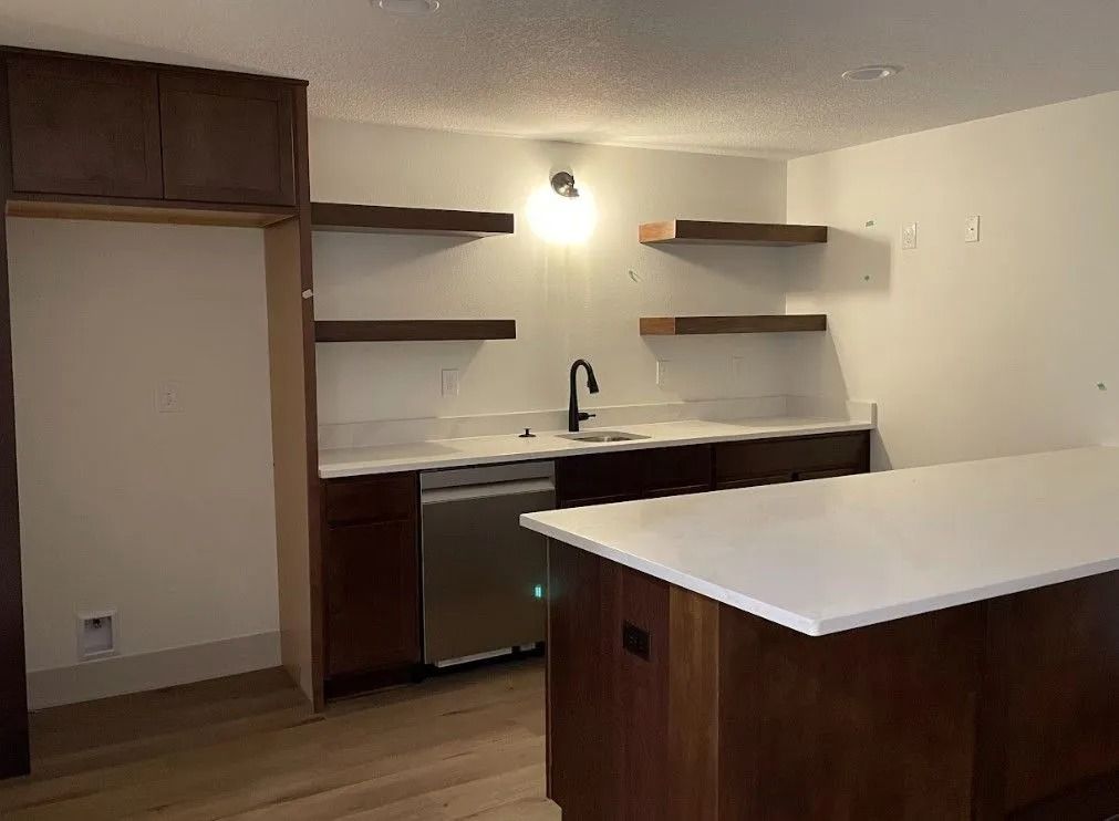 Modern kitchen with dark wood cabinets, stainless steel appliances, white countertop, and floating shelves.