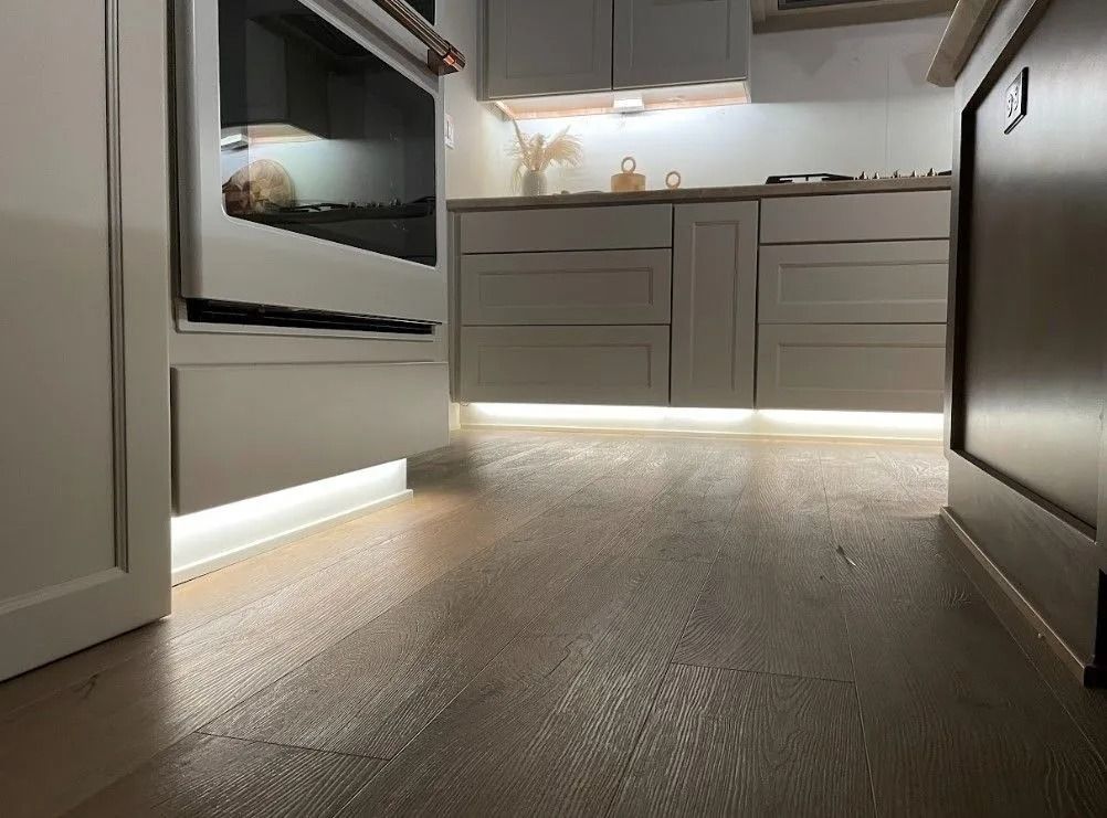 Kitchen with grey cabinets, under-cabinet lighting, and wood floor. Oven and dishwasher visible.