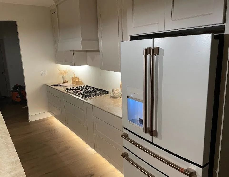 Modern kitchen with light cabinets, gas stovetop, and a white refrigerator with bronze handles.