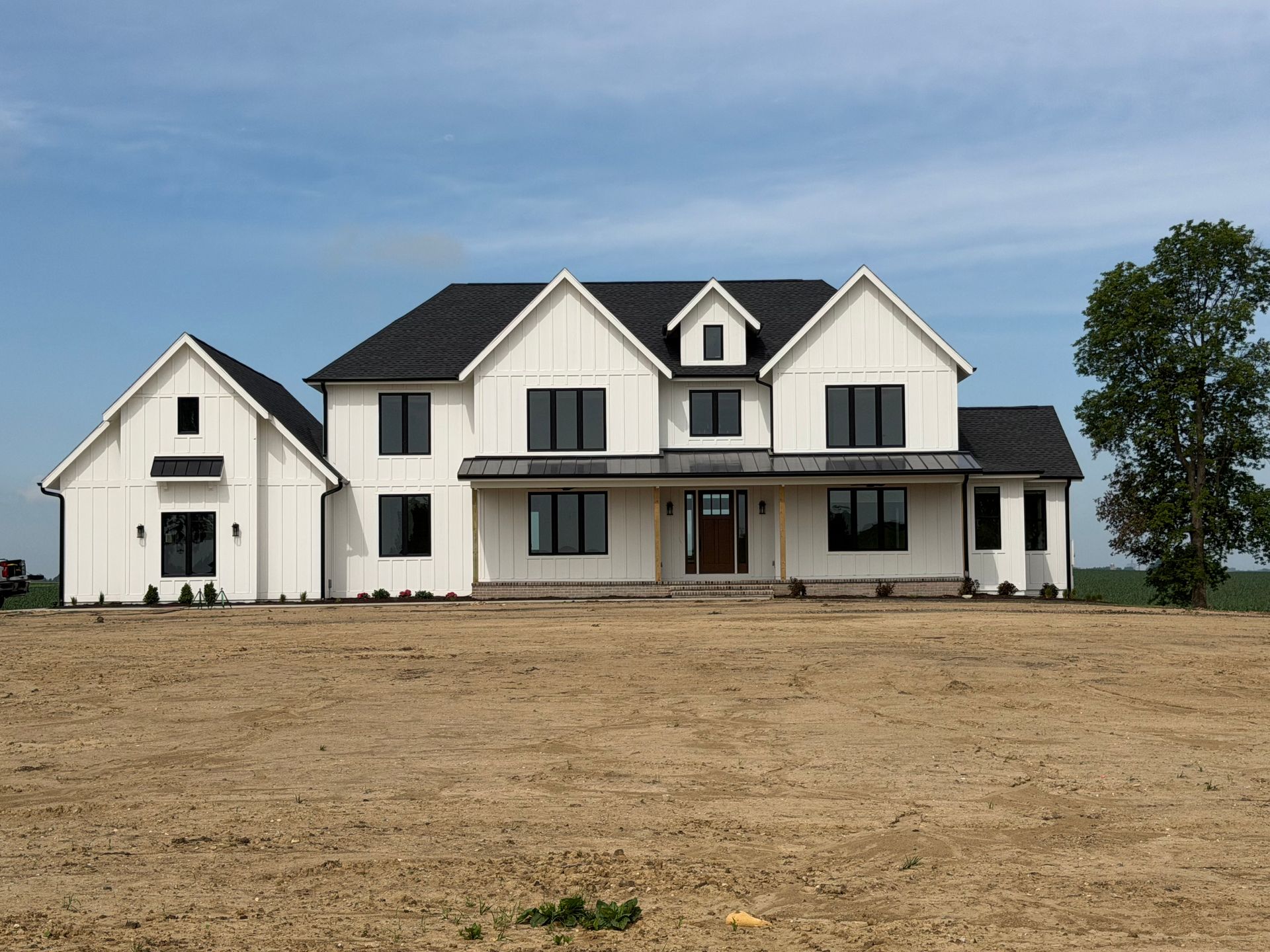 Large white two-story farmhouse with attached garage on a bare lot under a blue sky