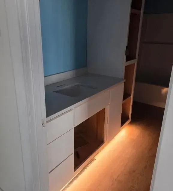 Narrow hallway with built-in white cabinets, gray countertop, and warm under-cabinet floor lighting