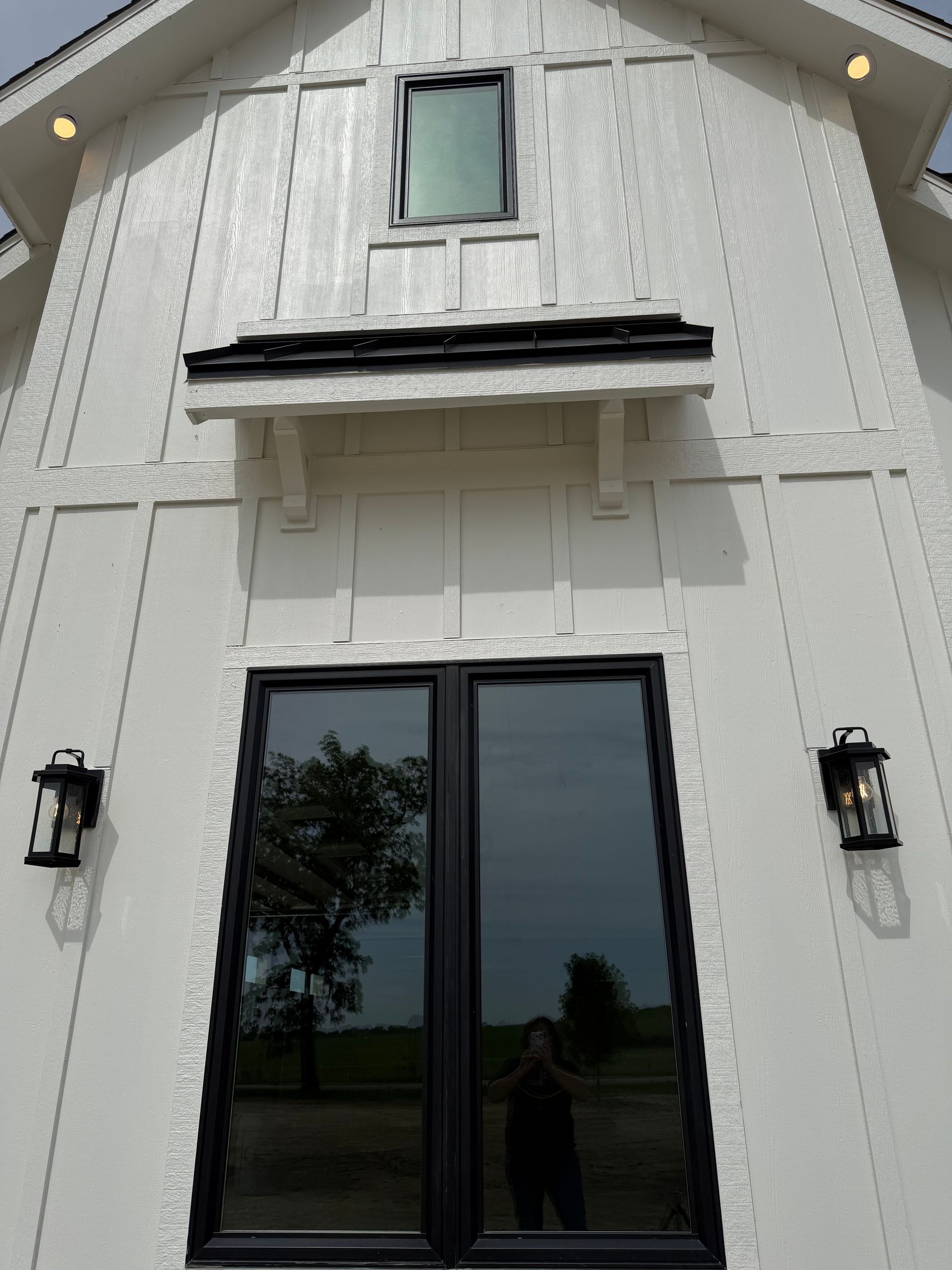 White house exterior with black double doors, wall lanterns, and a small upper window under a gabled roof