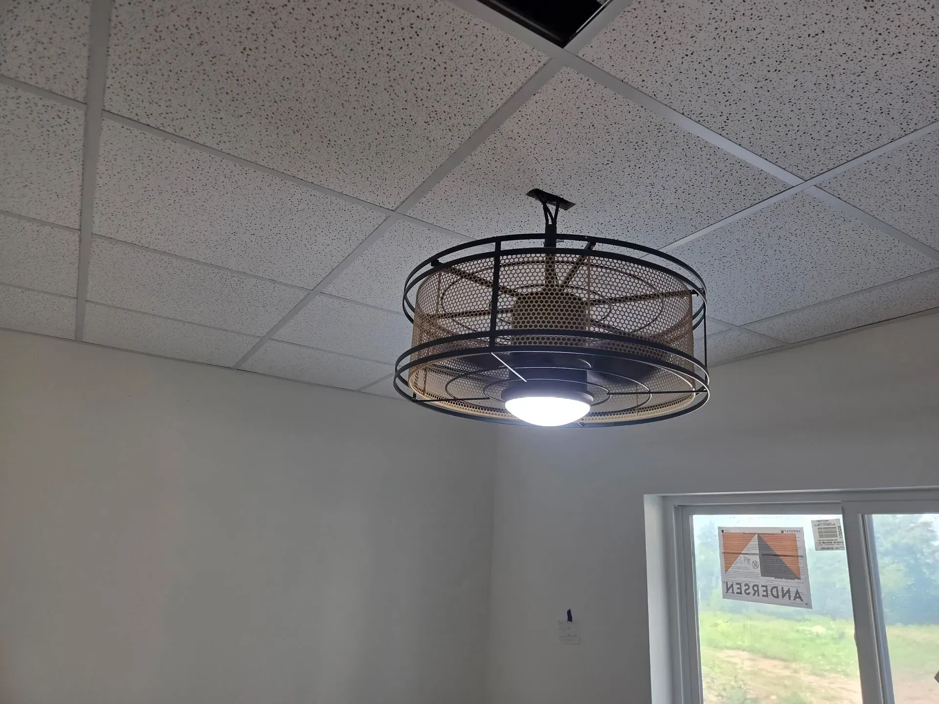 A room ceiling with a woven black chandelier and a bright window on the right.