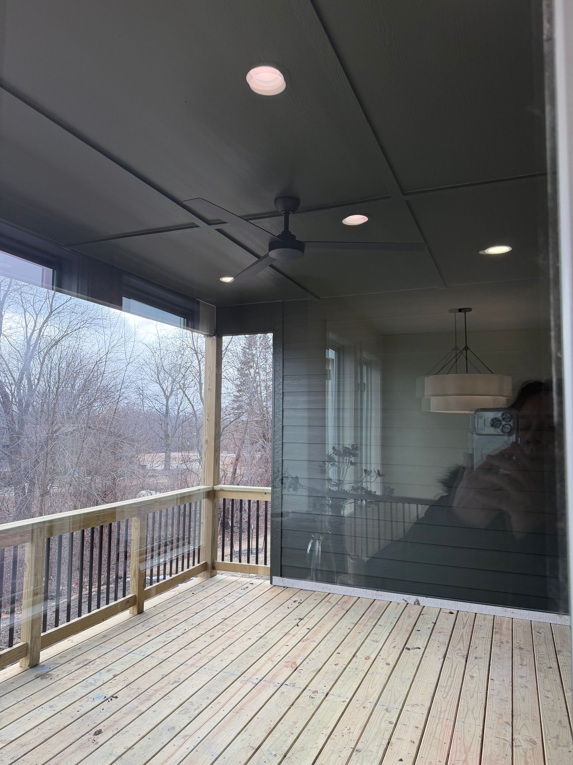Wooden deck with clear screens, ceiling fan, and recessed lighting. Overlooks a wooded area.