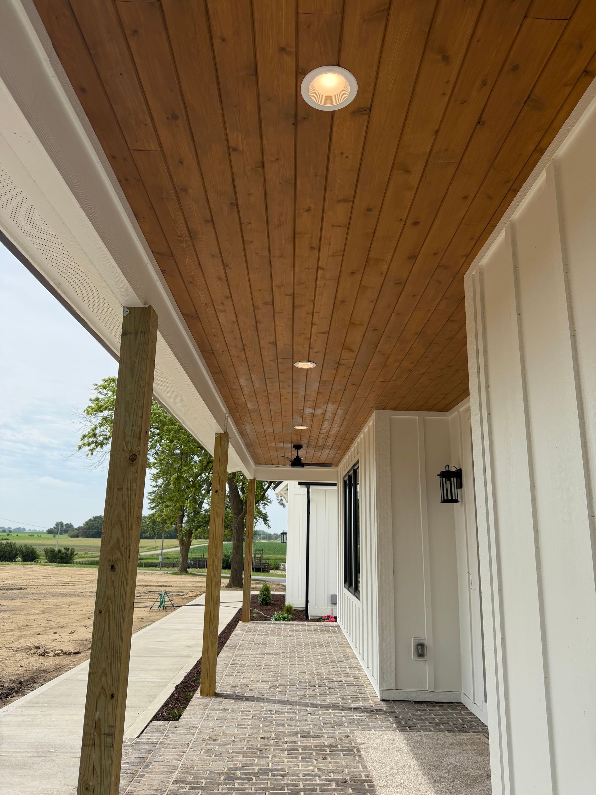 Covered porch with wood ceiling, white columns, and stone floor beside a field.