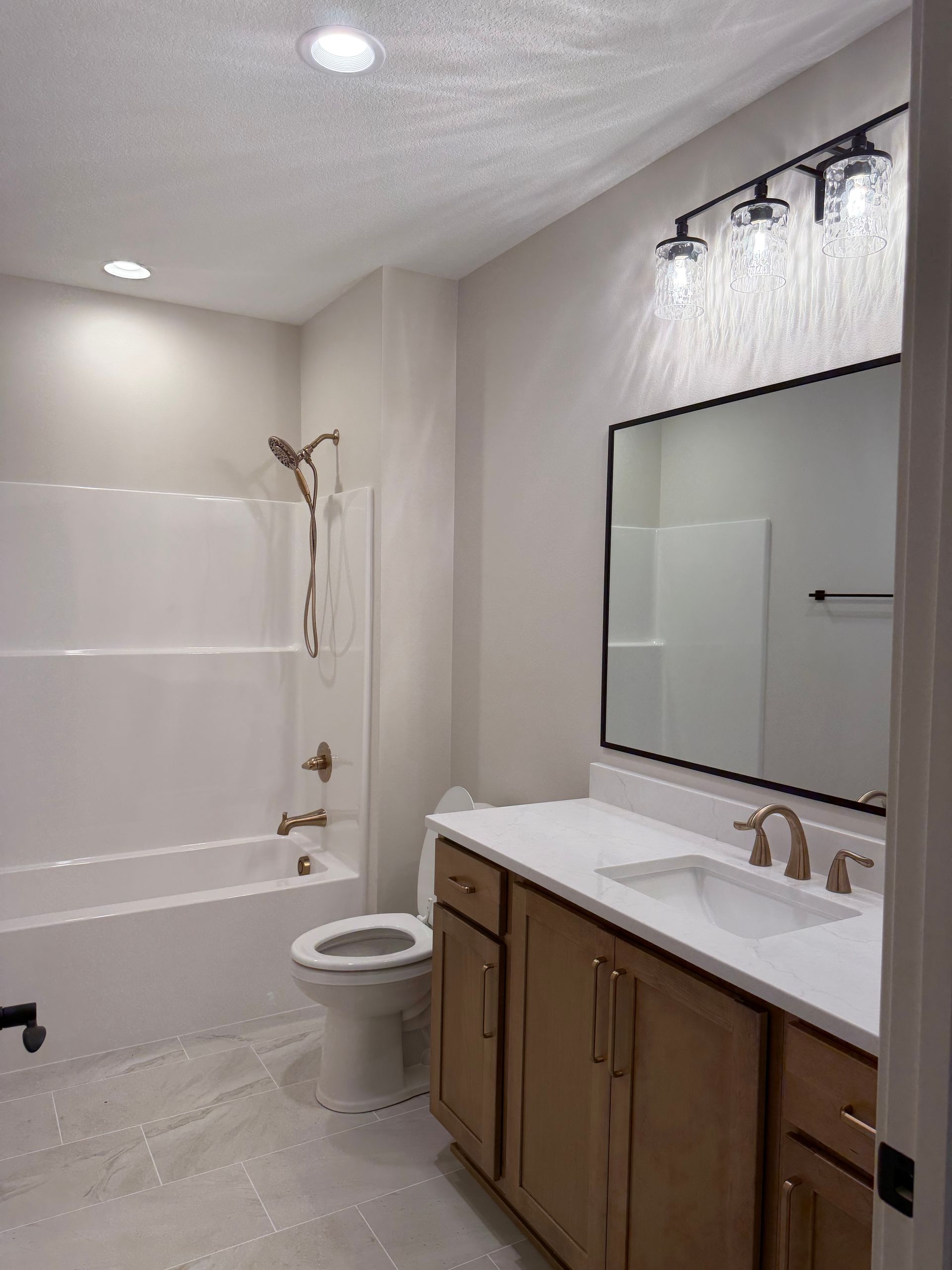 Bright bathroom with bathtub, toilet, vanity, large mirror, and bronze fixtures
