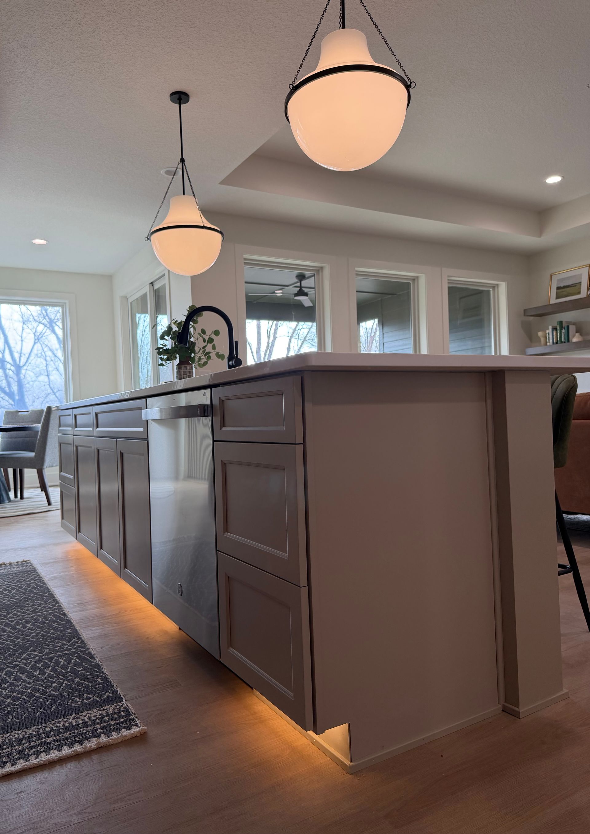 Kitchen island with pendant lights, cabinets, dishwasher, and warm under-cabinet lighting.