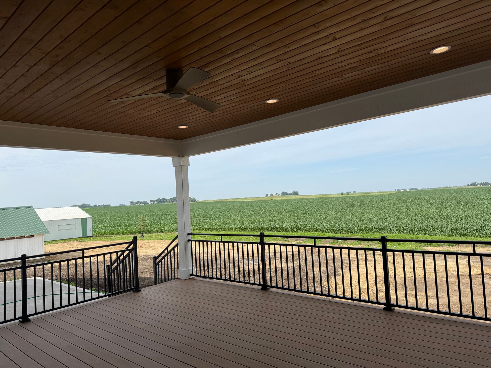 Covered porch overlooking green fields under a wooden ceiling