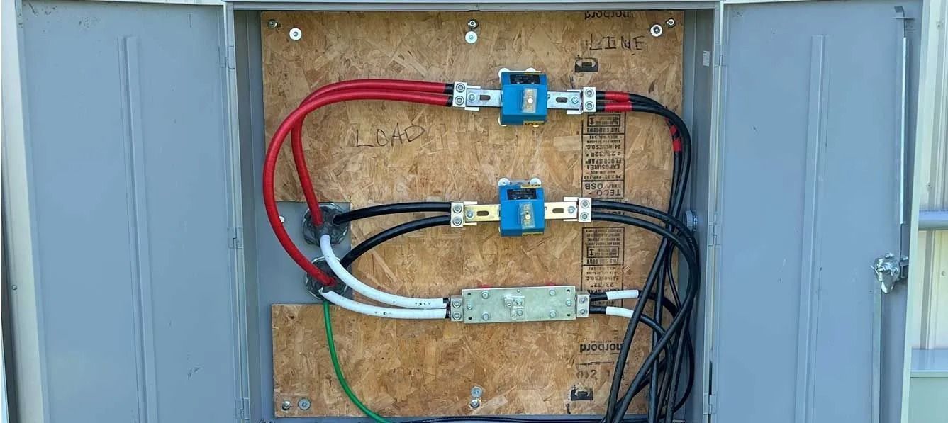 Open electrical panel with red, black, white, and green wires connected to blue and silver components on a wooden backing.