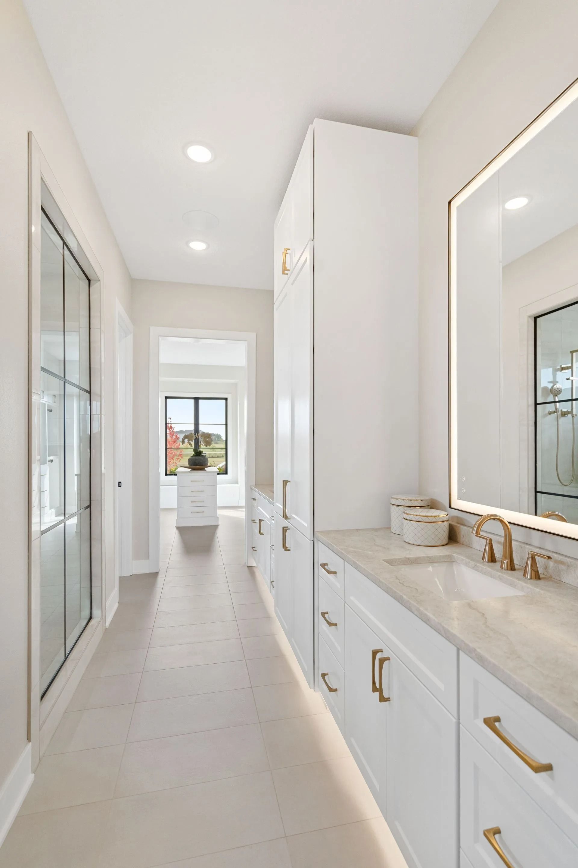 Long, white modern bathroom with a vanity, large mirror, and tall cabinet.