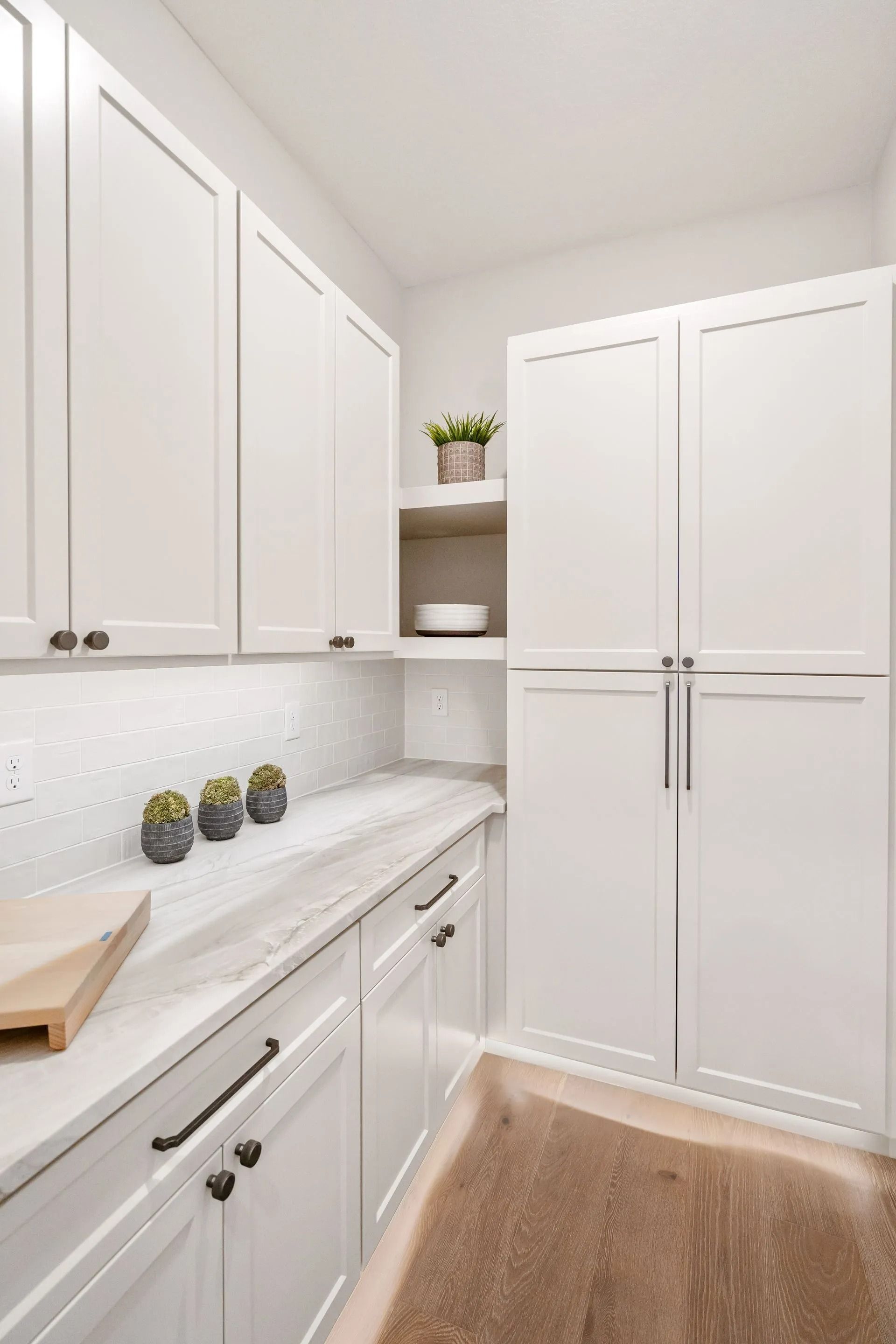 White kitchen pantry with cabinets, countertops, and wood flooring.