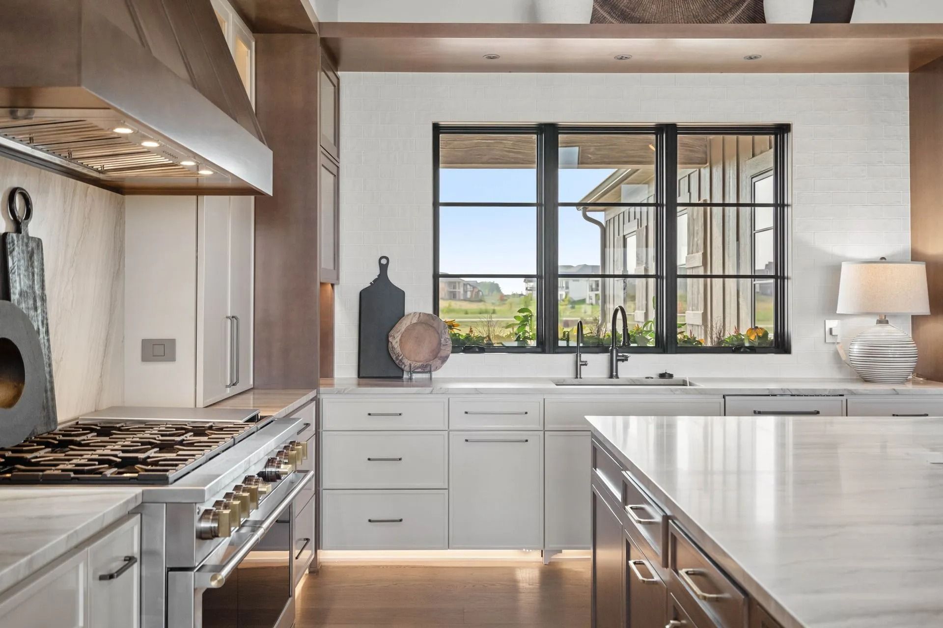 Modern kitchen with white cabinets, marble countertops, stainless steel appliances, and a window overlooking a green yard.