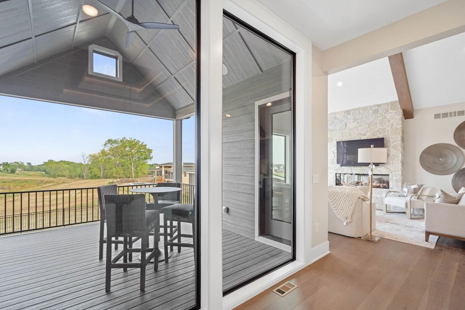 View through large glass door: outdoor deck with table and chairs; interior living room with fireplace.