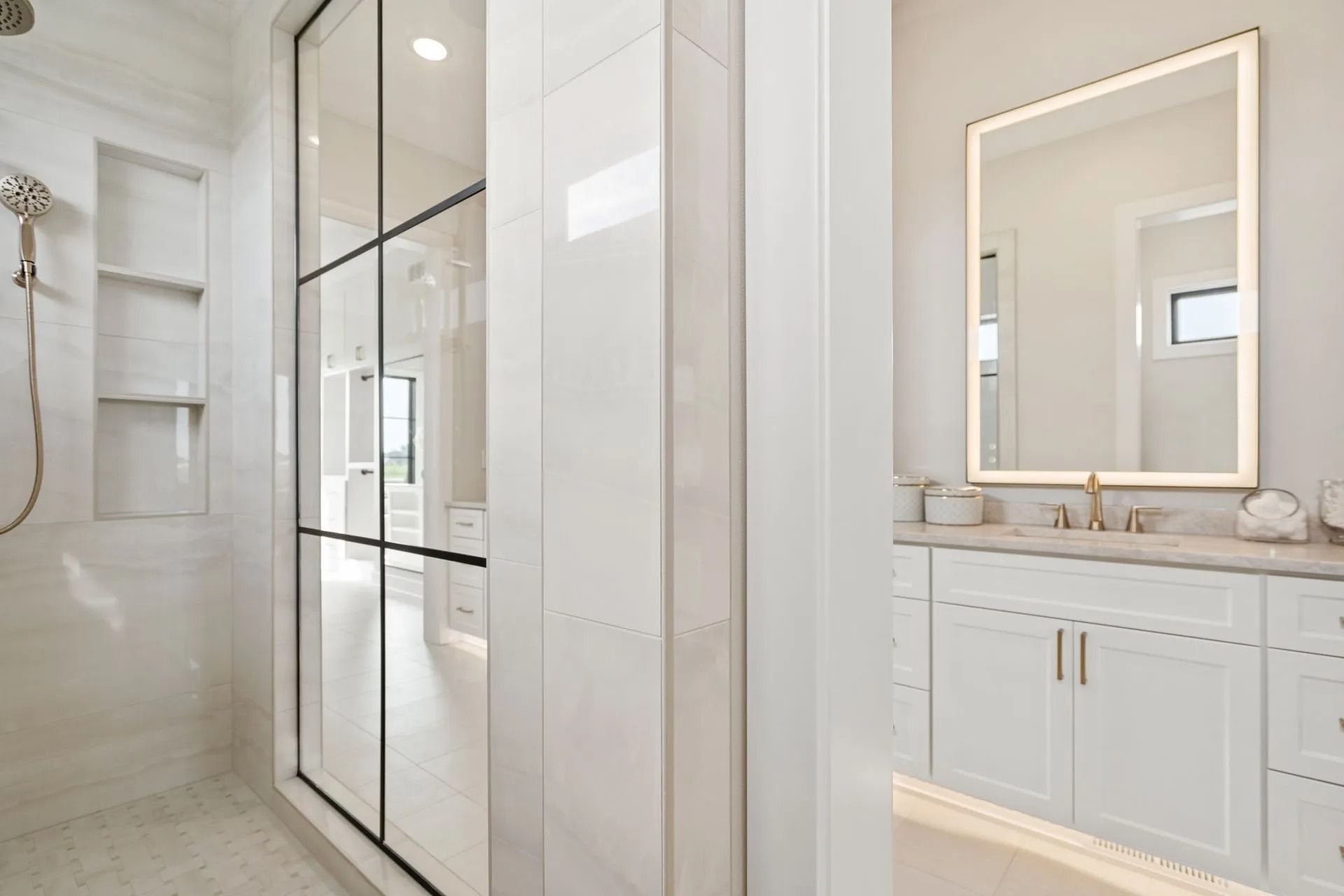 Modern white bathroom with glass shower, lit mirror, and marble vanity.