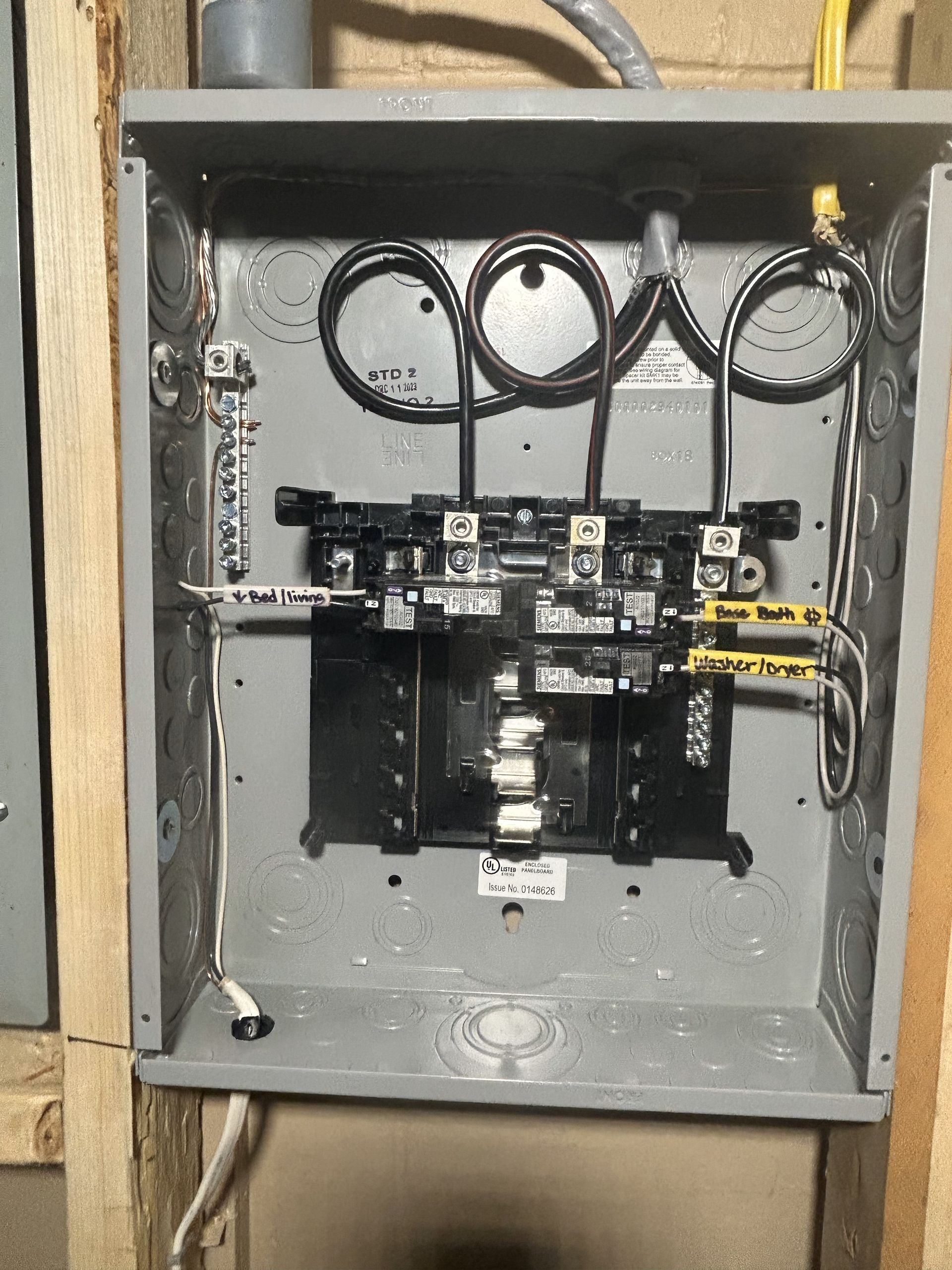 Open electrical panel with wires and circuit breakers. Gray box mounted on a wood wall.