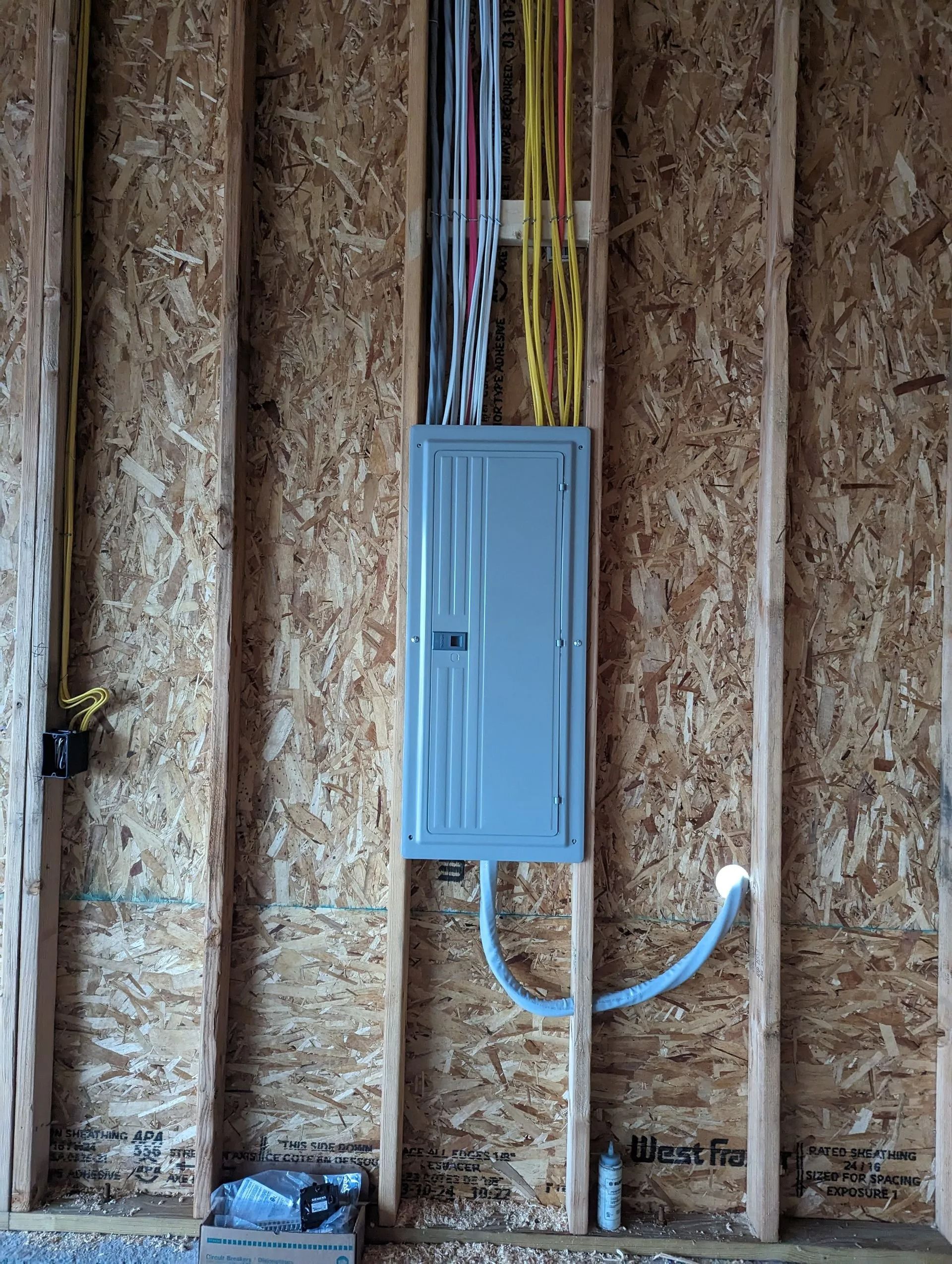 Electrical panel mounted on a wooden wall, with wires entering from above and conduit below.
