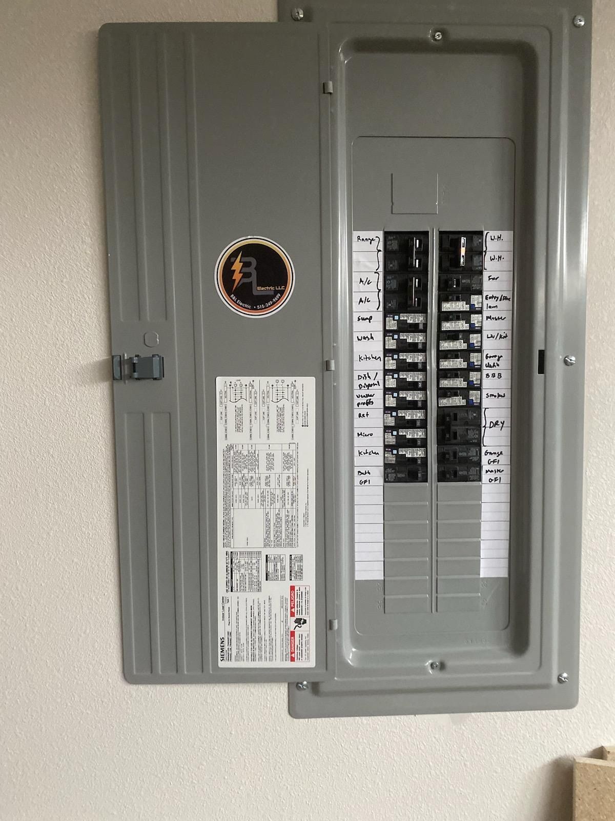 Opened gray electrical panel with circuit breakers on white wall.