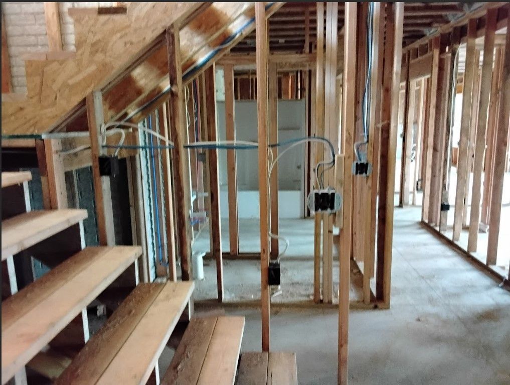 Interior view of a building under construction, showing wooden framing, electrical wiring, and a staircase.