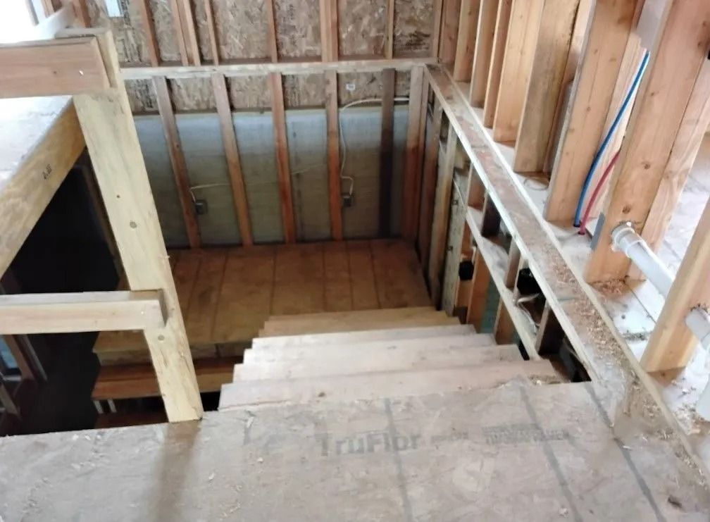 Wooden staircase under construction, framed walls, unfinished plywood steps.