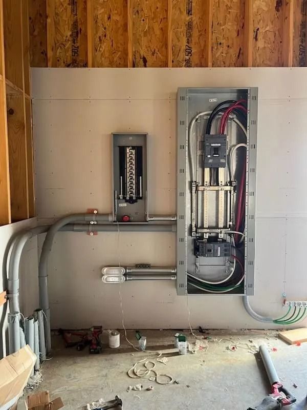 Electrical panel installation with conduit and wiring on a drywall wall in a construction site.