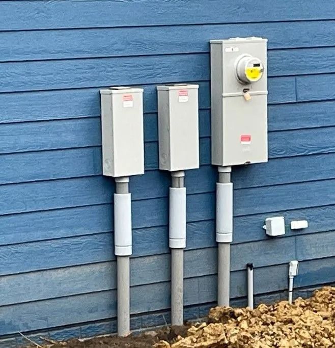 Three electrical boxes mounted on a blue wall; a meter, and two unmarked boxes, all on gray conduits.