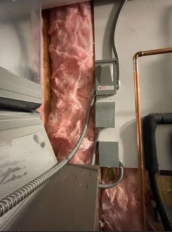 Electrical boxes and metal conduit in wall cavity with pink insulation. Copper pipe visible.