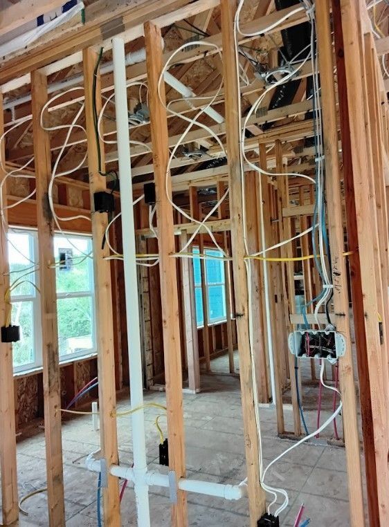 Interior view of a building frame with electrical wiring and plumbing pipes installed, before drywall.
