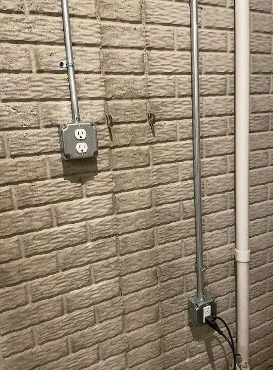 Electrical outlets and conduit on a brick wall. Gray metal boxes and conduits, white brick.