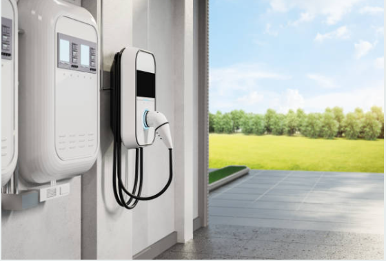 EV charging stations mounted on a wall with a cable connected, set outside near grass and trees.
