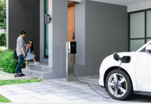 Man and child enter home. Electric car charging in driveway. Gray exterior.