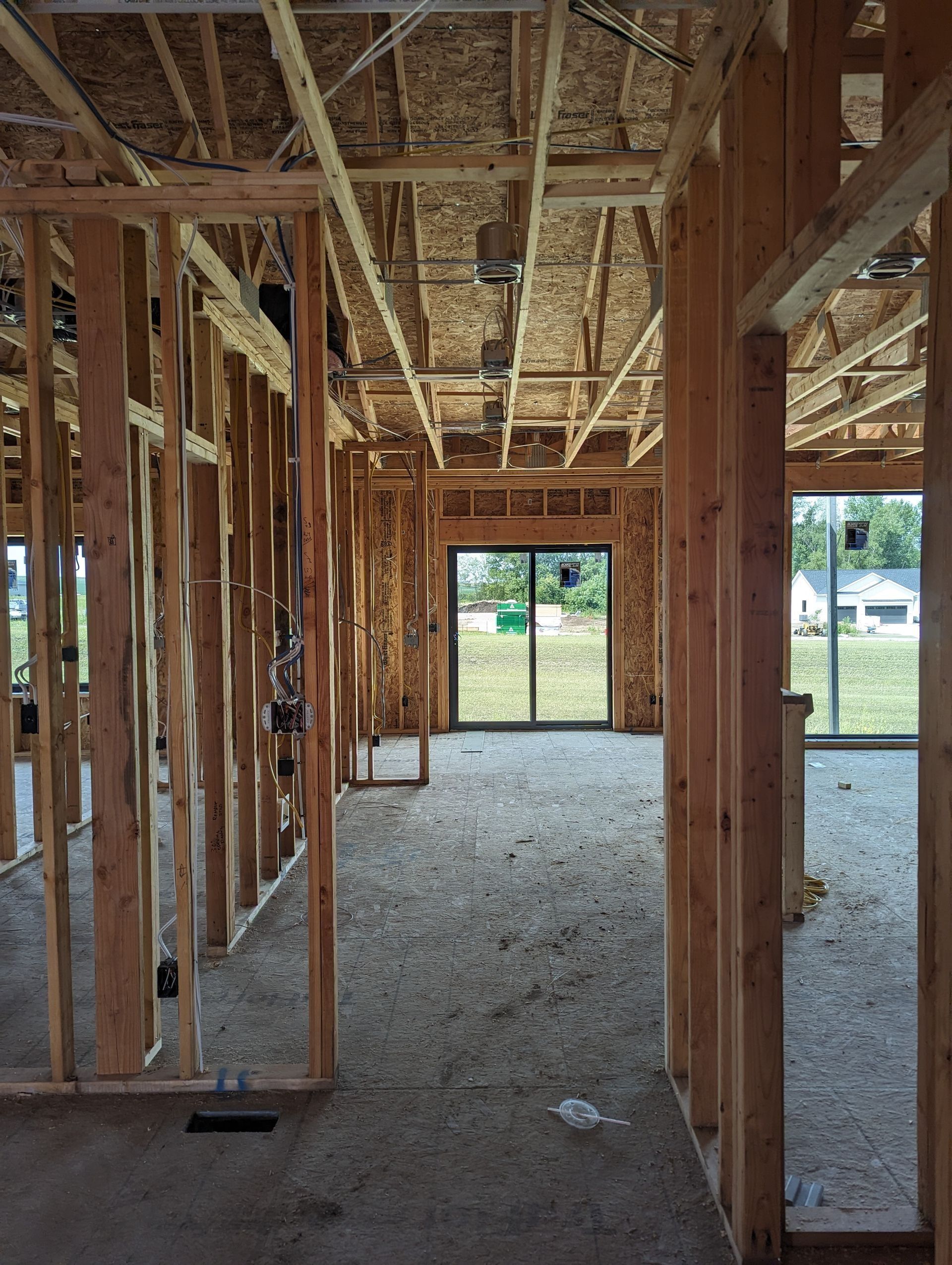 Interior view of a building under construction, showing wooden framing, open spaces, and an exterior door.
