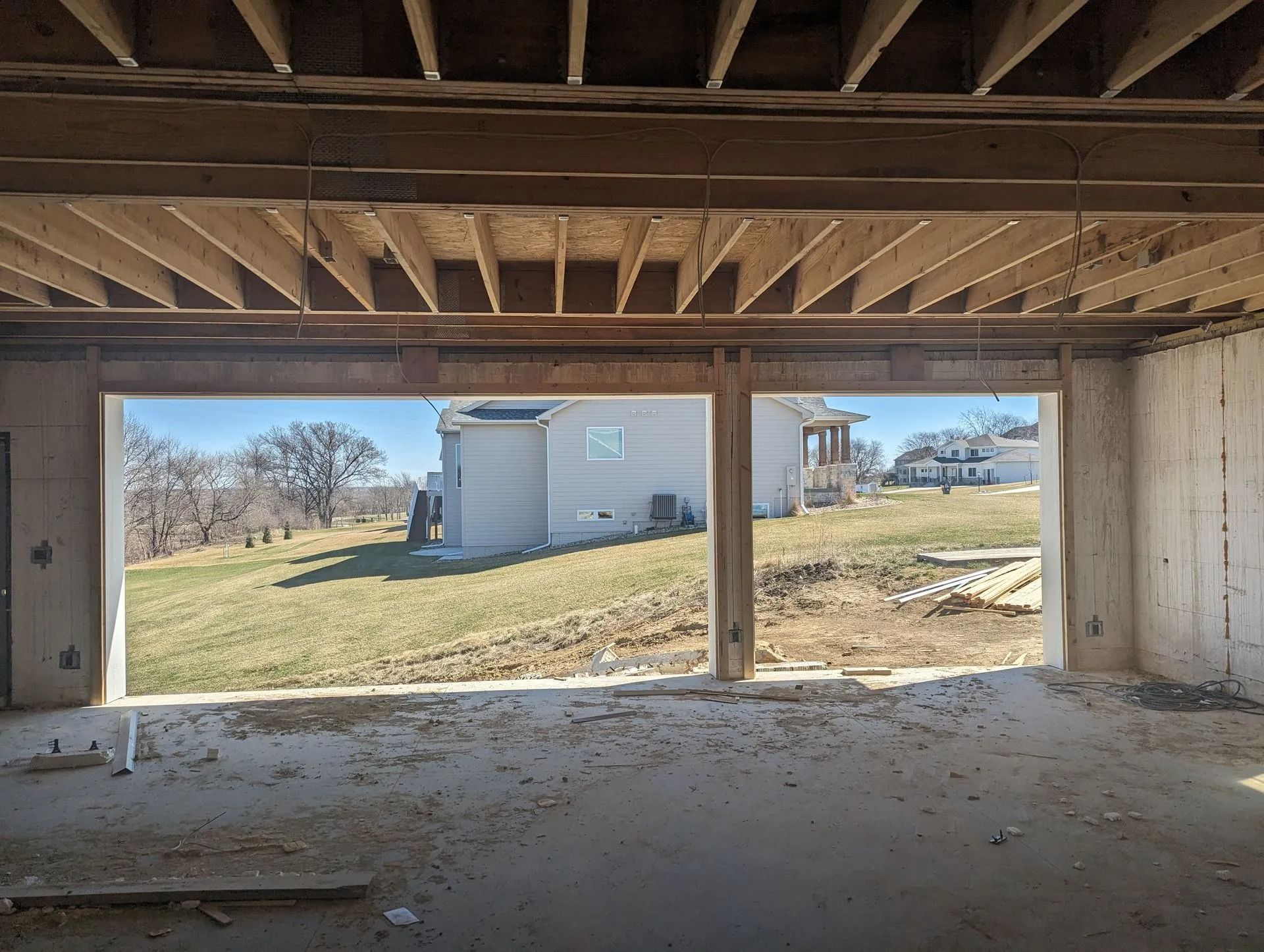 View of a grassy backyard through unfinished doorway openings in a concrete basement. Blue sky.