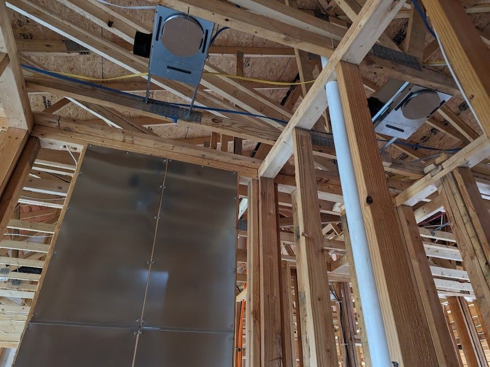Interior view of a building under construction, showing wooden framing, ductwork, and metal panels.