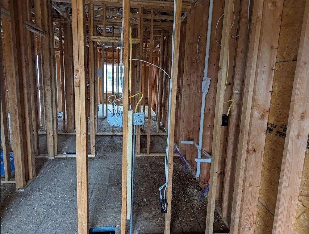 Interior view of a building under construction, showing wooden framing with electrical wiring and outlets.