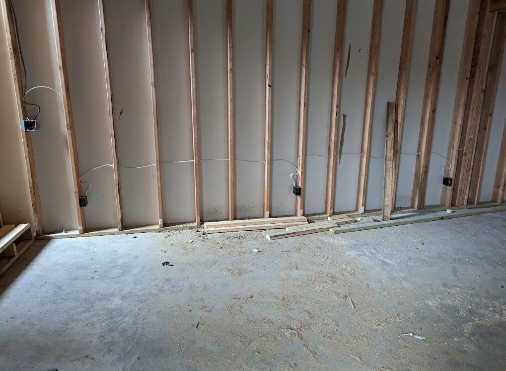 Interior view of a room under construction with exposed wooden studs, electrical boxes, and a concrete floor.