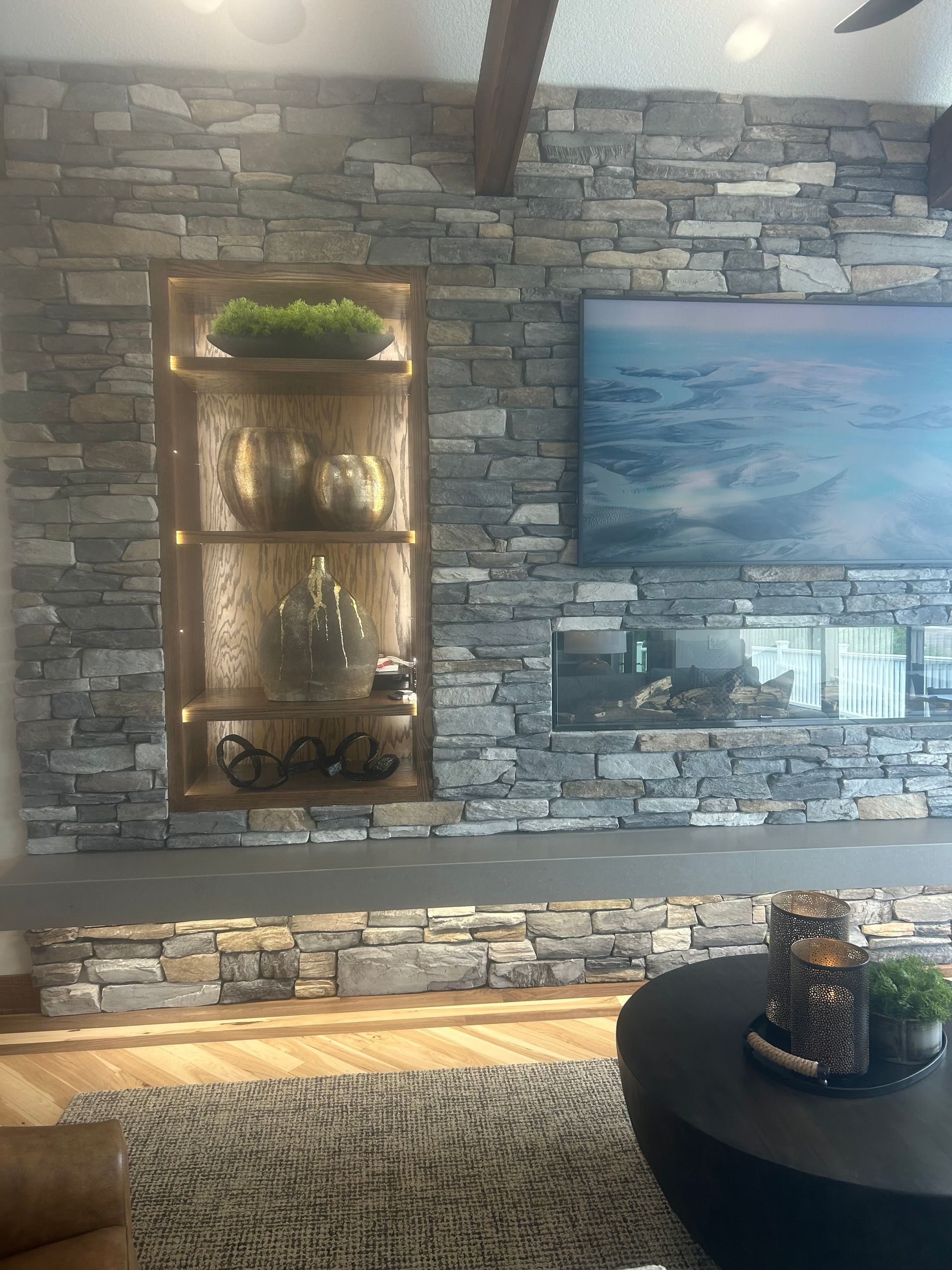 Stone wall with built-in display case and fireplace; TV above fireplace, modern living room.