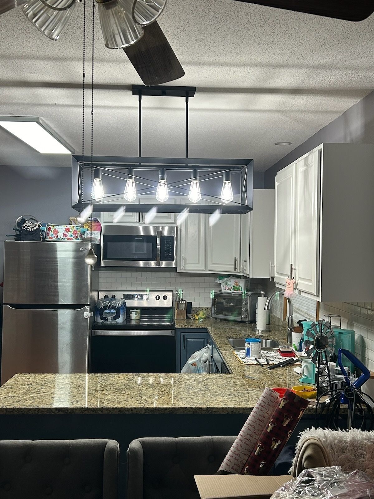 Kitchen interior with a rectangular light fixture over a countertop. Stainless steel appliances and white cabinets are visible.