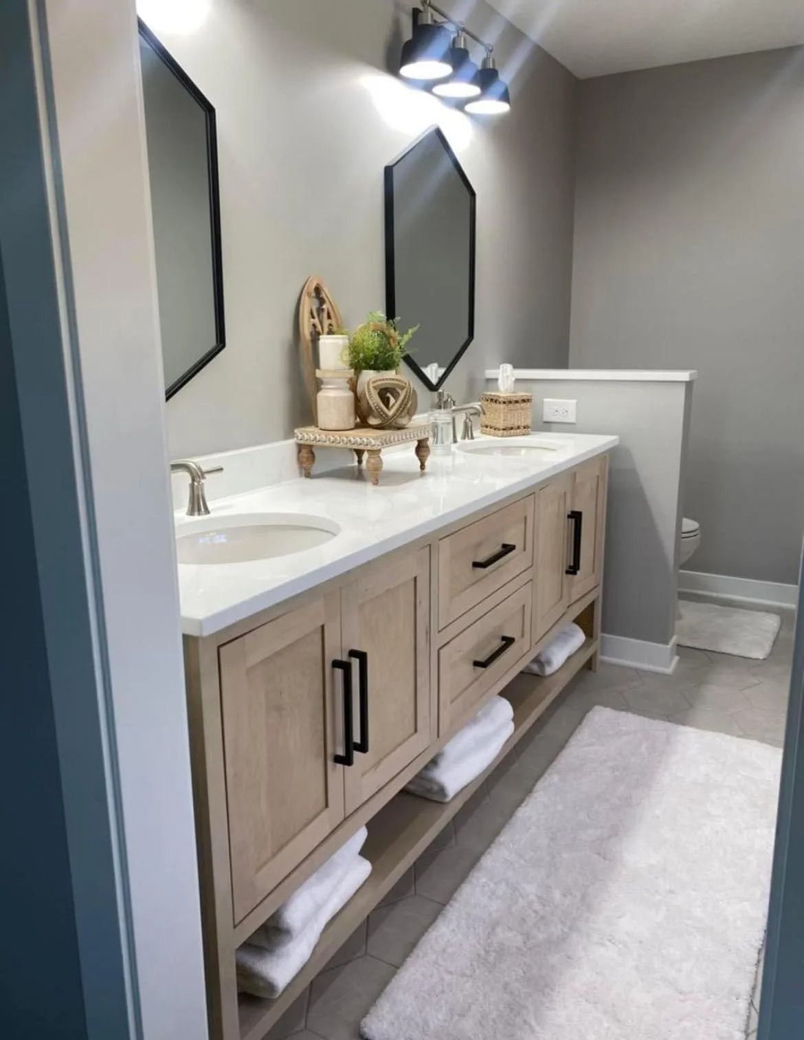 Bathroom with double vanity, light wood cabinets, black hardware, hexagon mirrors, and white countertop.