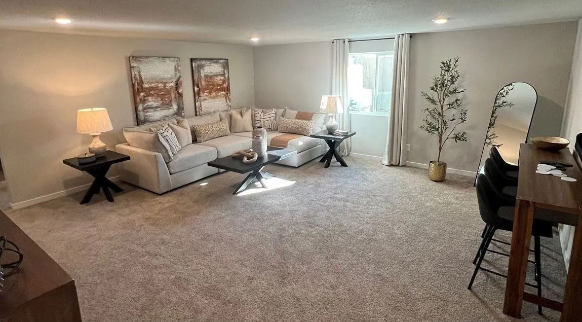 Living room with a large light-colored sectional sofa, dark tables, artwork, and a tall mirror.