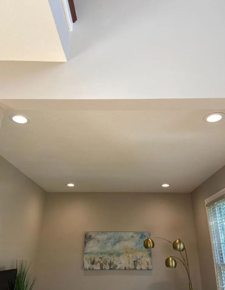 Ceiling with recessed lights, artwork, and a gold floor lamp in a living room.