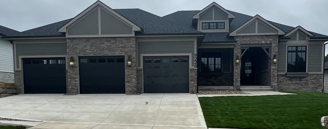 Modern home with dark garage doors, stone accents, and green siding.