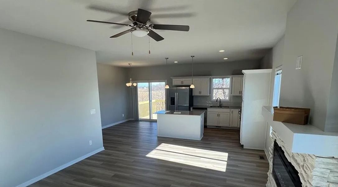 Open-concept living space with kitchen island, light gray walls, wood-look floors, and ceiling fan.