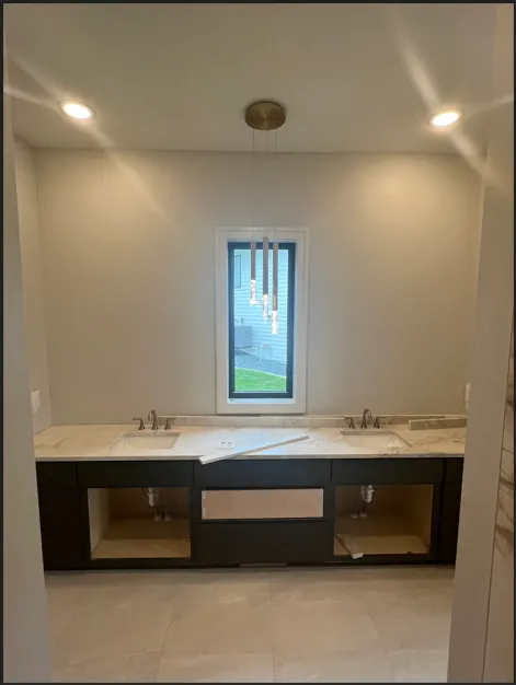 Bathroom under construction with dark cabinets, light countertops, window, and overhead lighting.