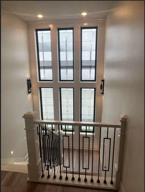 View from above a staircase with windows above. White walls, black window frames, and decorative wrought iron.
