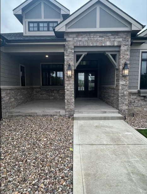 Stone and gray-sided house exterior with covered porch, concrete walkway, and double glass doors.