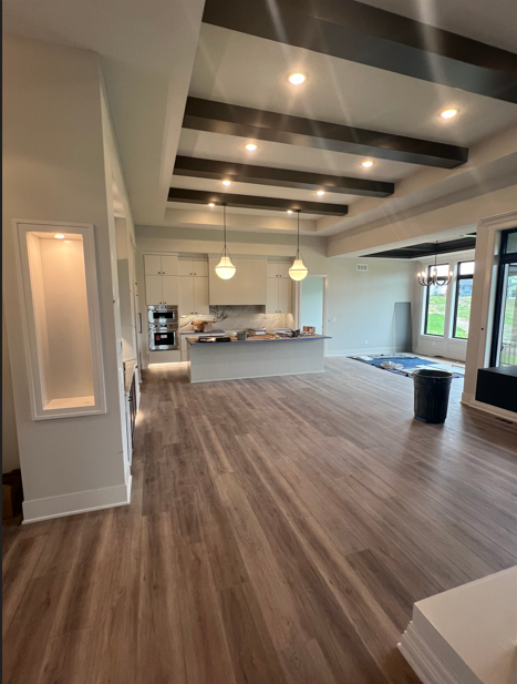 Spacious interior with wood floors, recessed ceiling lights, and dark wood beams. Kitchen island and large windows.