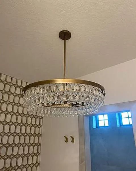 Gold and crystal chandelier hangs from a ceiling, with a patterned wall to the left and a doorway to the right.