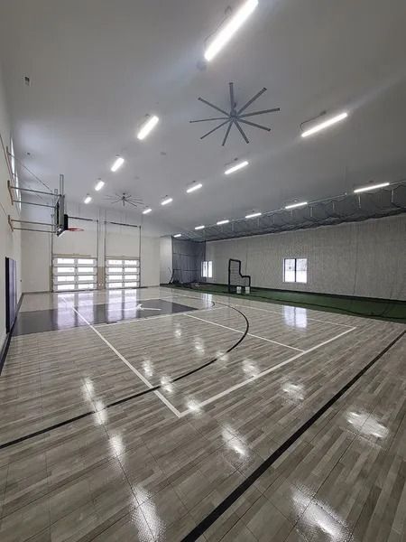 Indoor basketball court with wooden floor, white lines, hoop, and large ceiling fan.