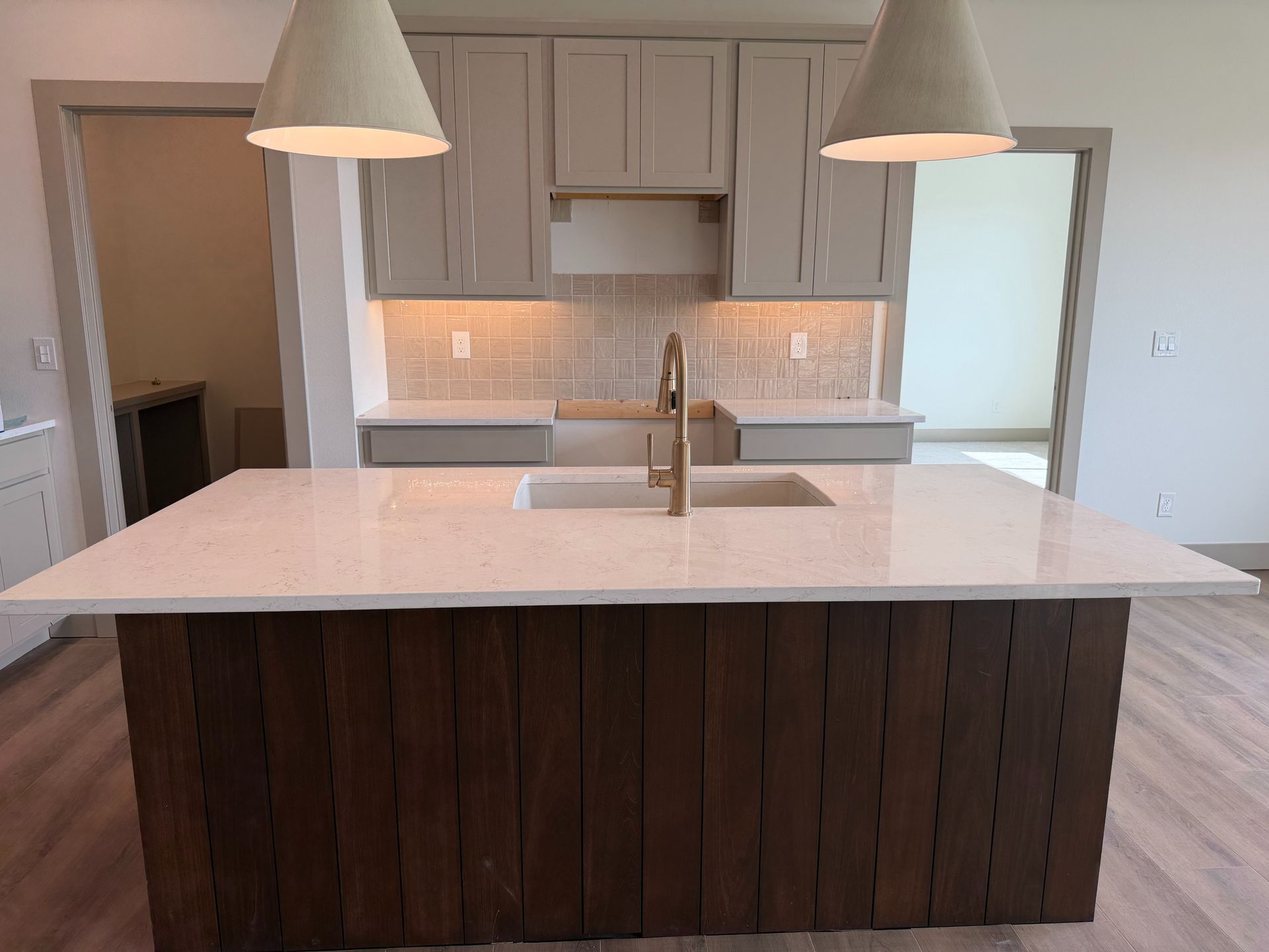 Modern kitchen island with white countertop, dark wood base, and two pendant lights under soft lighting